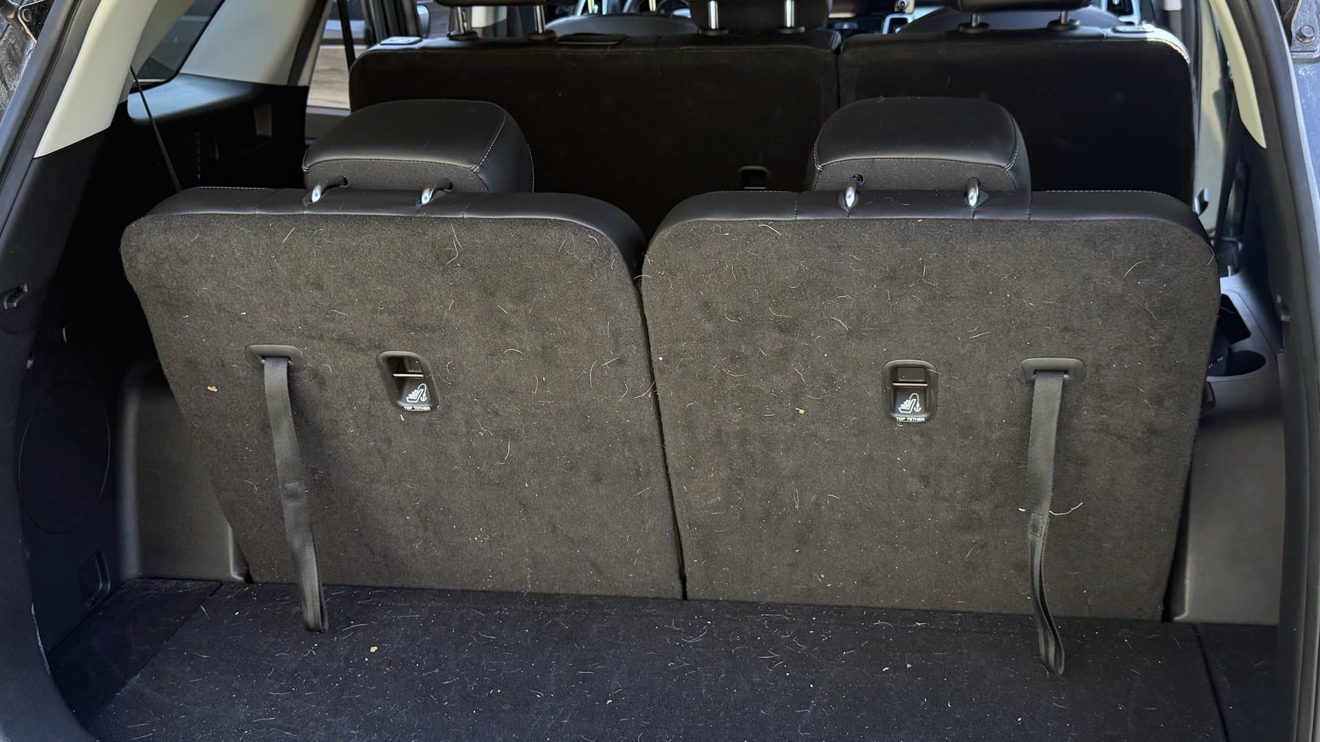 An SUV cargo area before detailing — rear seats and carpet dusty and covered in debris